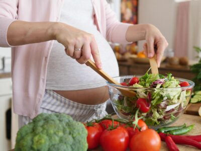 Pregnant Woman Mixing Fresh Green Salad On Kitchen. Closeup.