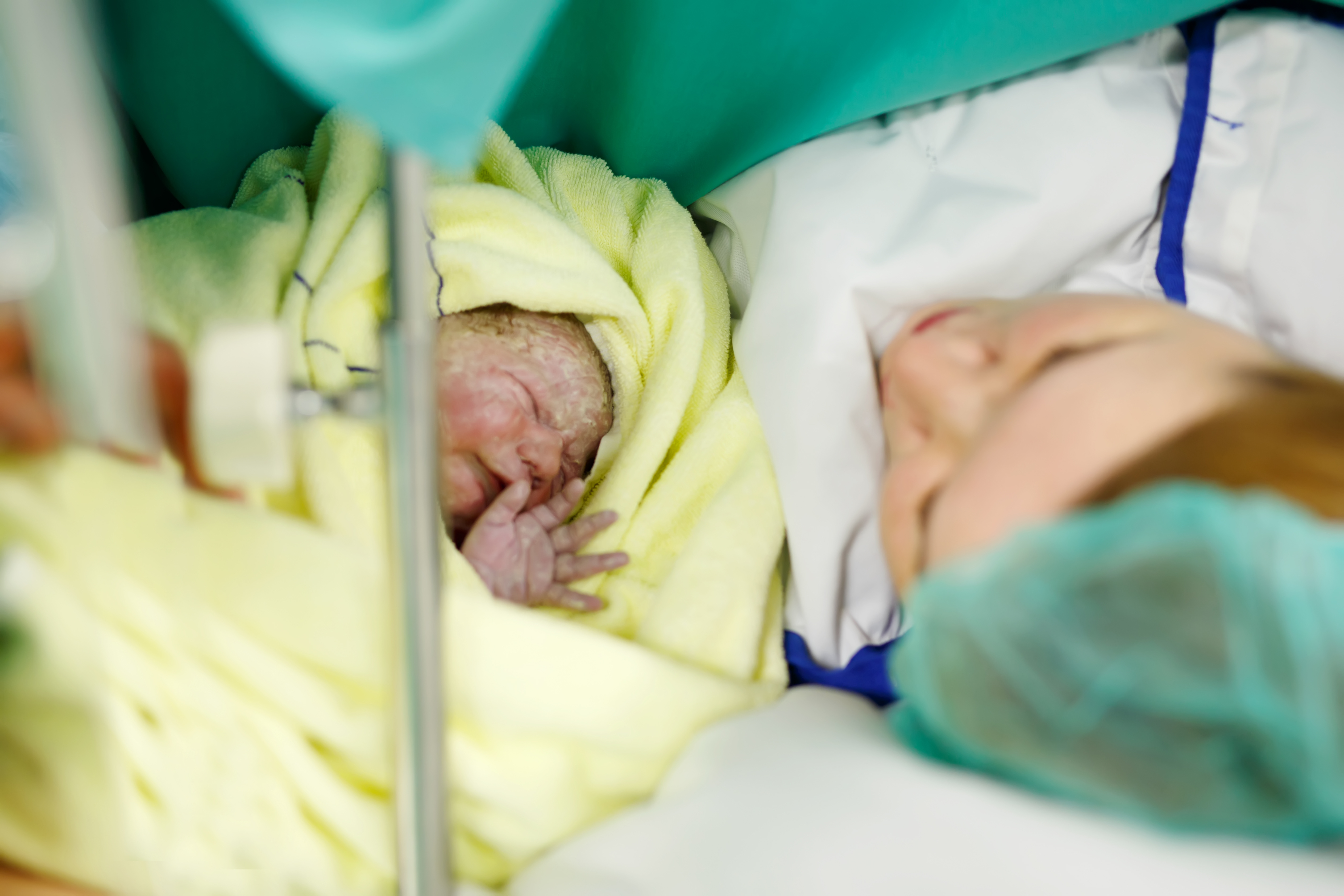 Newborn baby wrapped in blankets after birth. Mother looking for the first time on new born daughter. Newborn child seconds and minutes after birth. Happy mum crying.